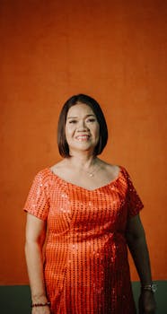 Smiling woman in an elegant orange dress against a simple backdrop, showcasing fashion and beauty.
